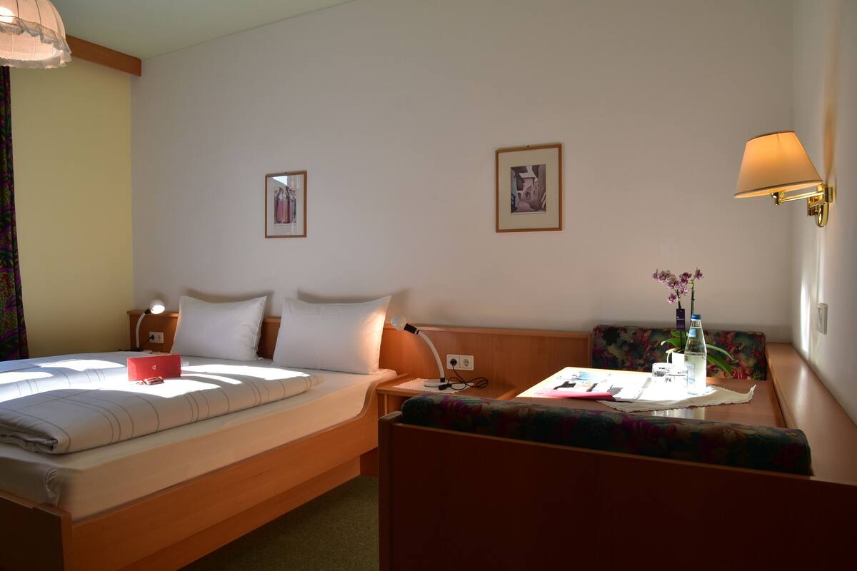 Une chambre d’hôtel avec un lit, une table de chevet, une lampe et une petite table sur laquelle se trouvent un vase et une bouteille.
