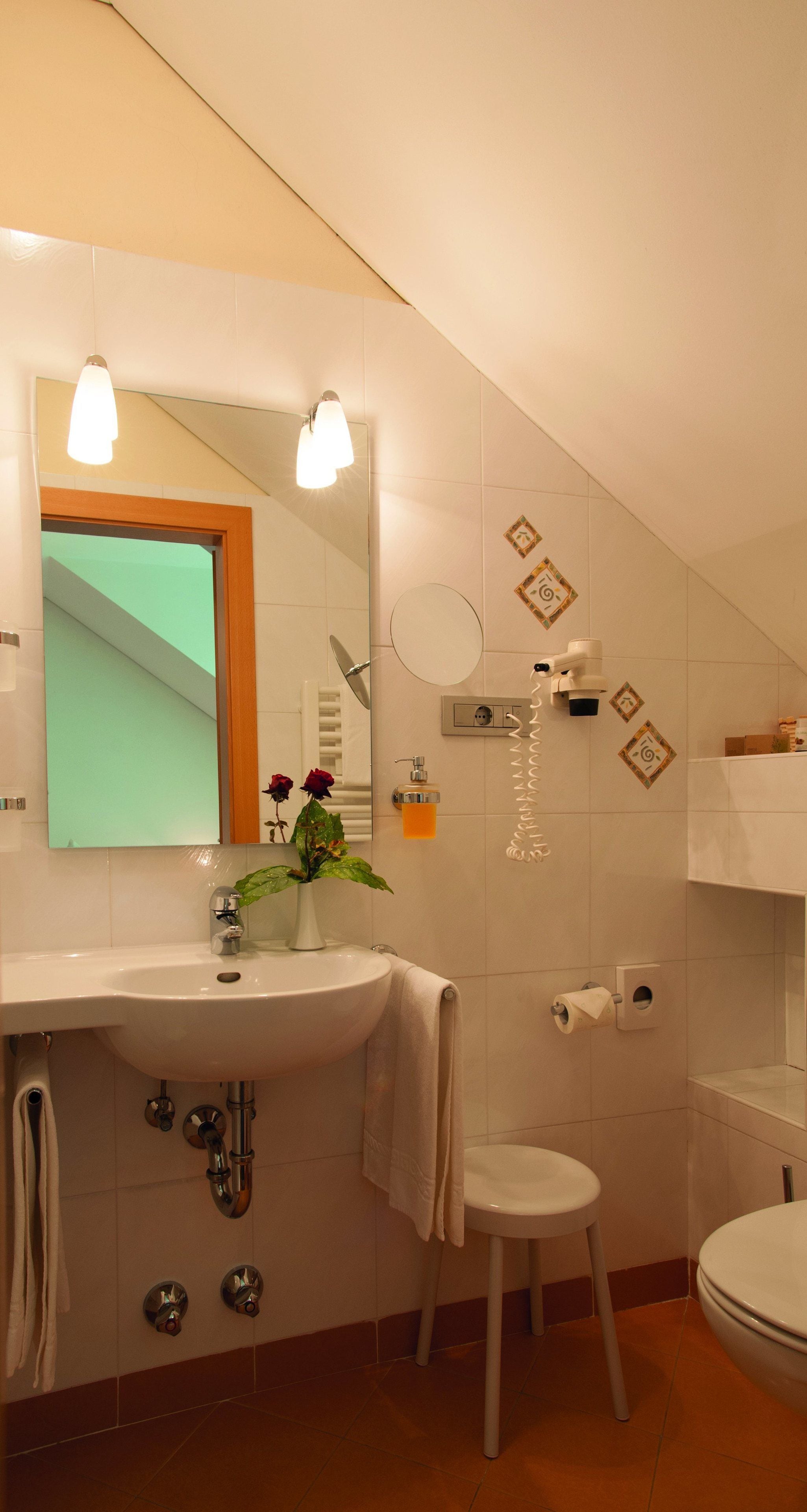 A bathroom with a sink, mirror, towel rack, toilet, and a small stool.