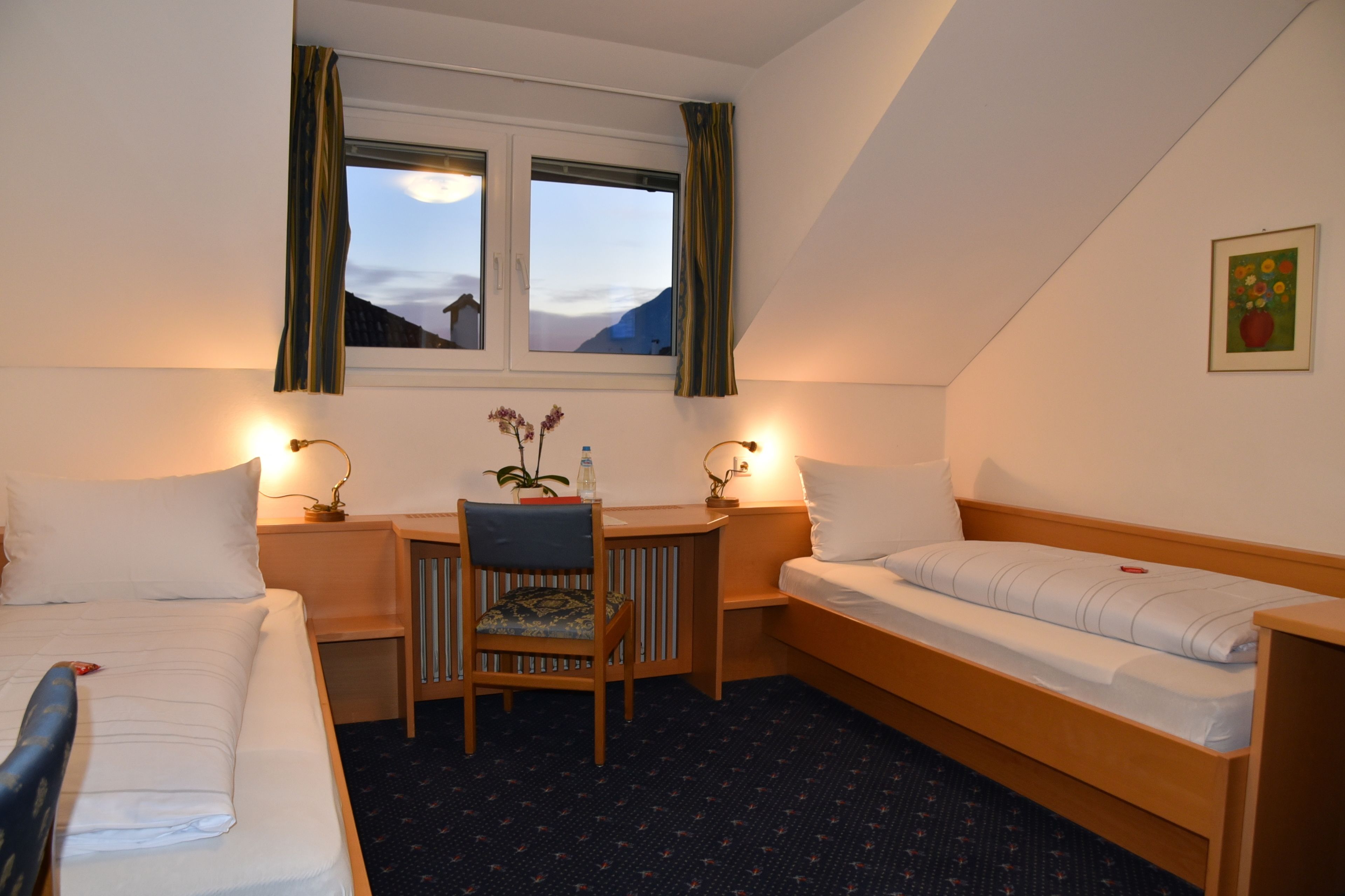 Habitación de hotel con cama, escritorio, silla y ventana con cortinas.