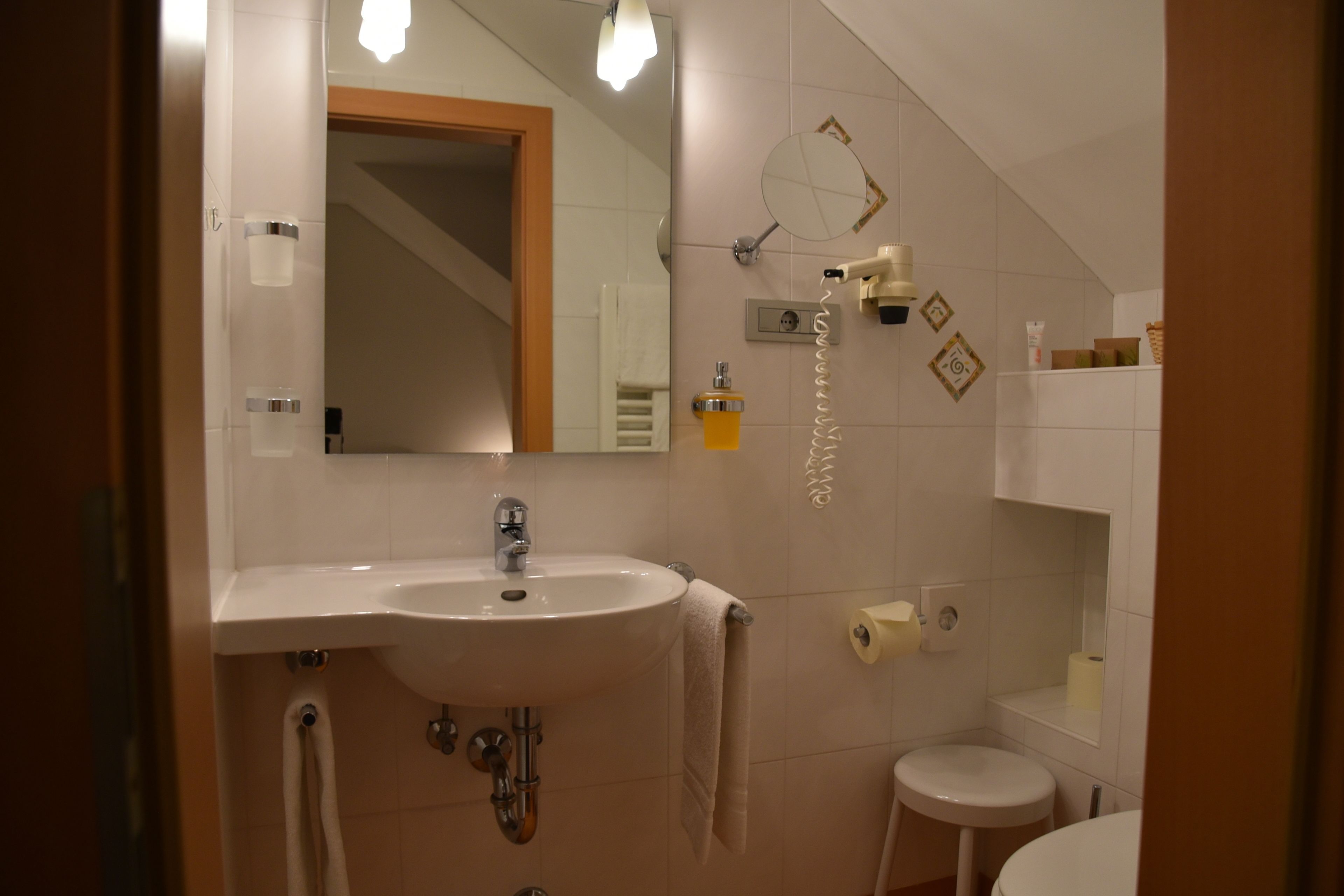 Une salle de bain équipée d’un lavabo, d’un miroir, d’un porte-serviettes, de toilettes et d’une petite étagère où sont rangés les articles de toilette.