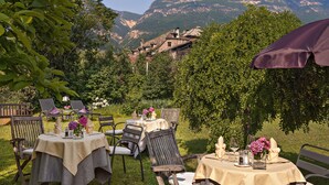 Un espace de restauration en plein air, avec des tables disposées pour deux personnes, entouré d’une végétation luxuriante et offrant une vue sur un paysage montagneux.