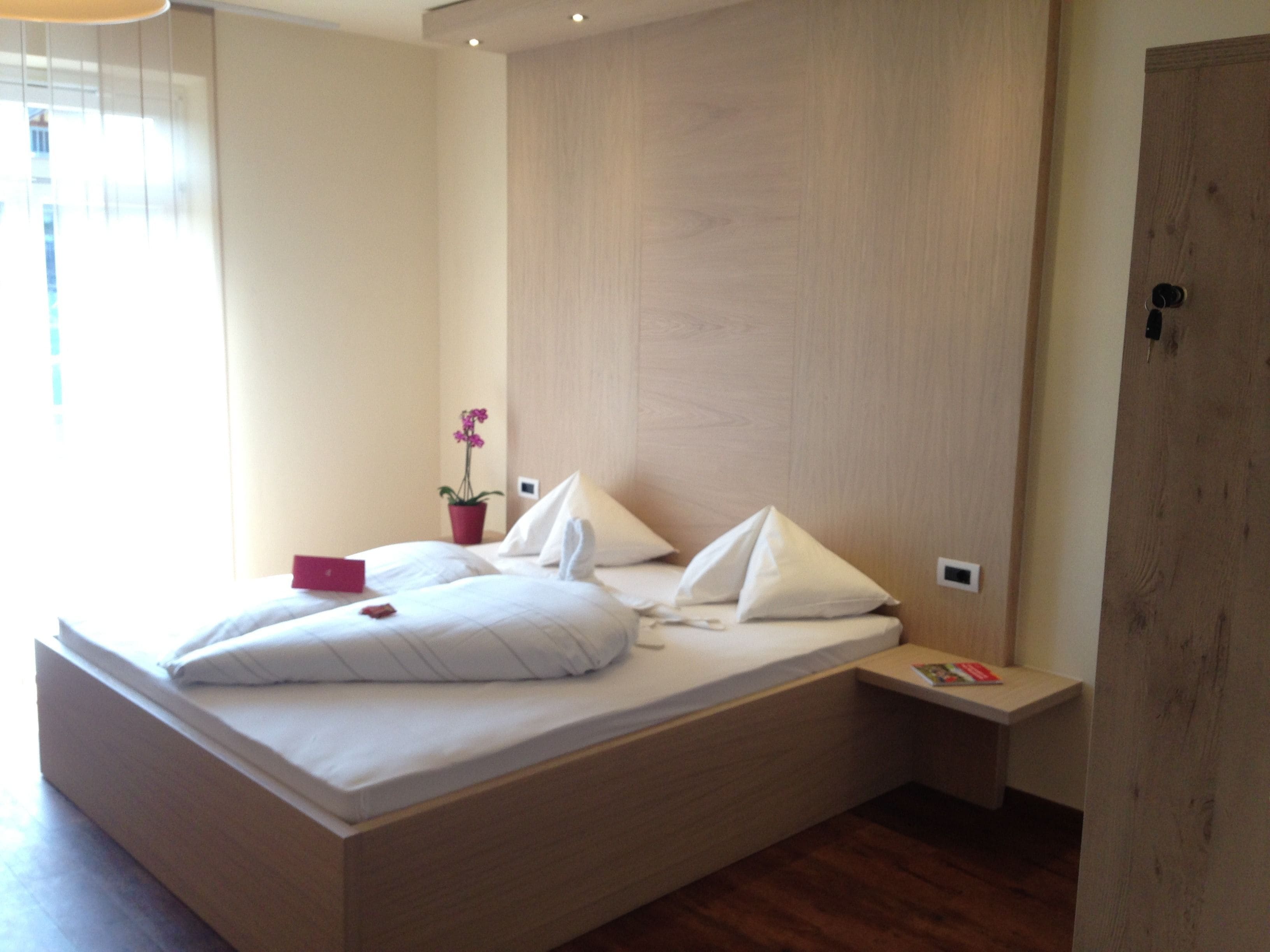 A modern bedroom with a built-in bed, a bedside table, a potted plant, and a wooden wardrobe.