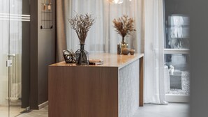 A modern kitchen with a central island, pendant lighting, and a view of the living area through a glass door.