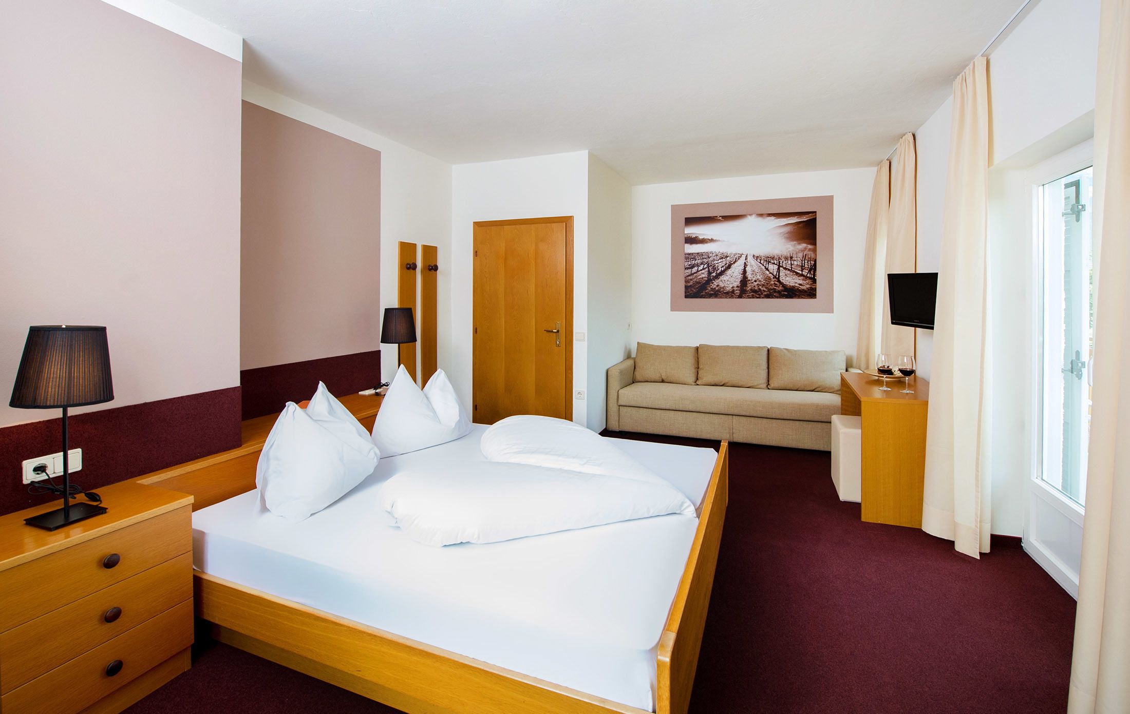 A hotel room with a bed, a sofa, a TV, and a window with curtains.