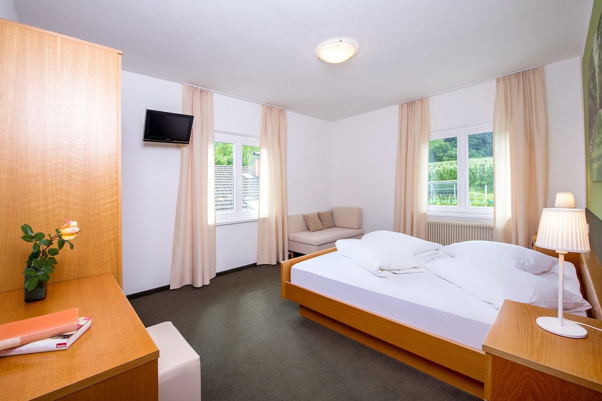 A hotel room with a bed, a sofa, a TV, and a desk with a lamp.