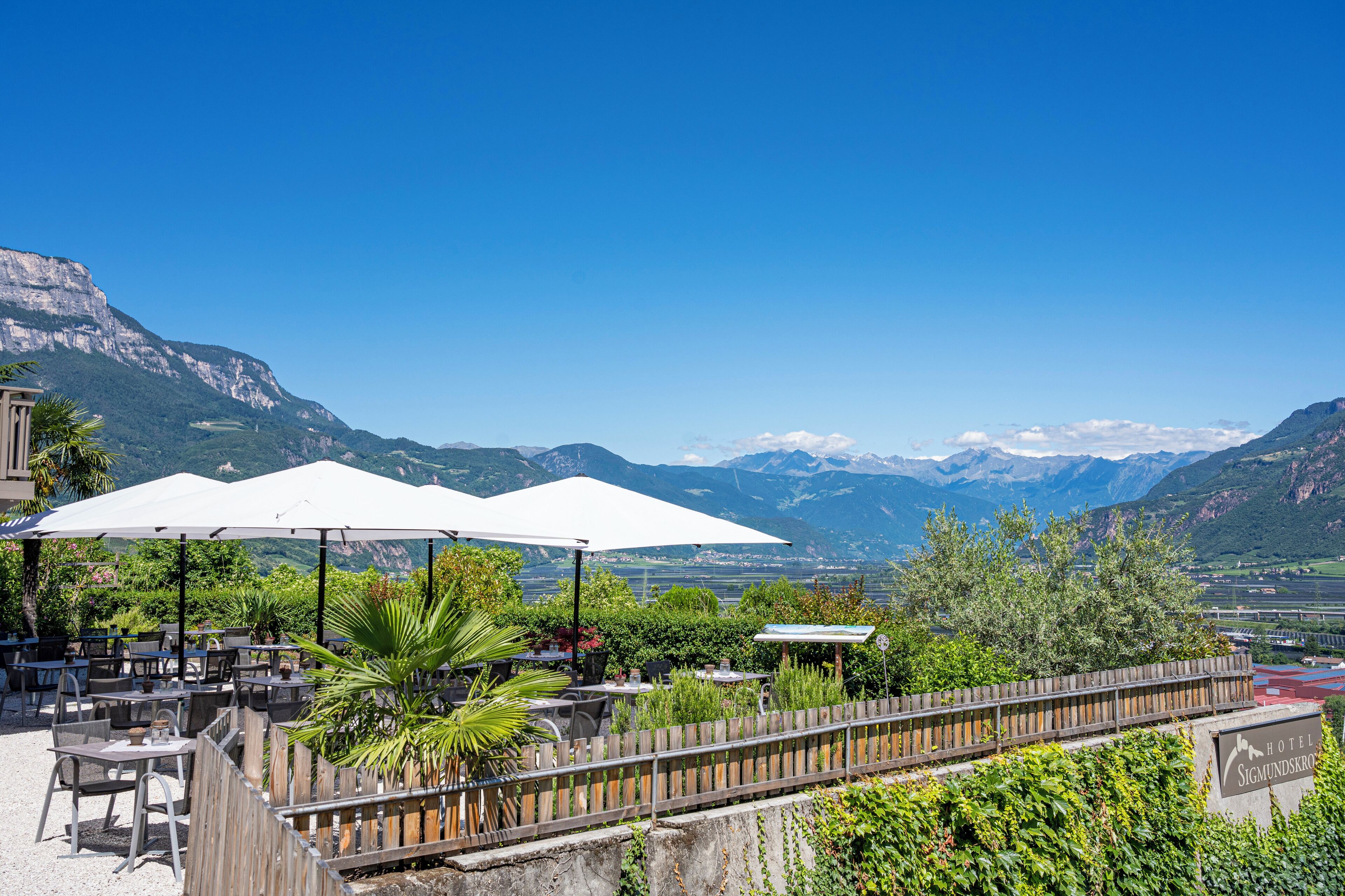 Eine Terrasse mit Sitzgelegenheiten im Freien, weißen Sonnenschirmen und Blick auf Berge.