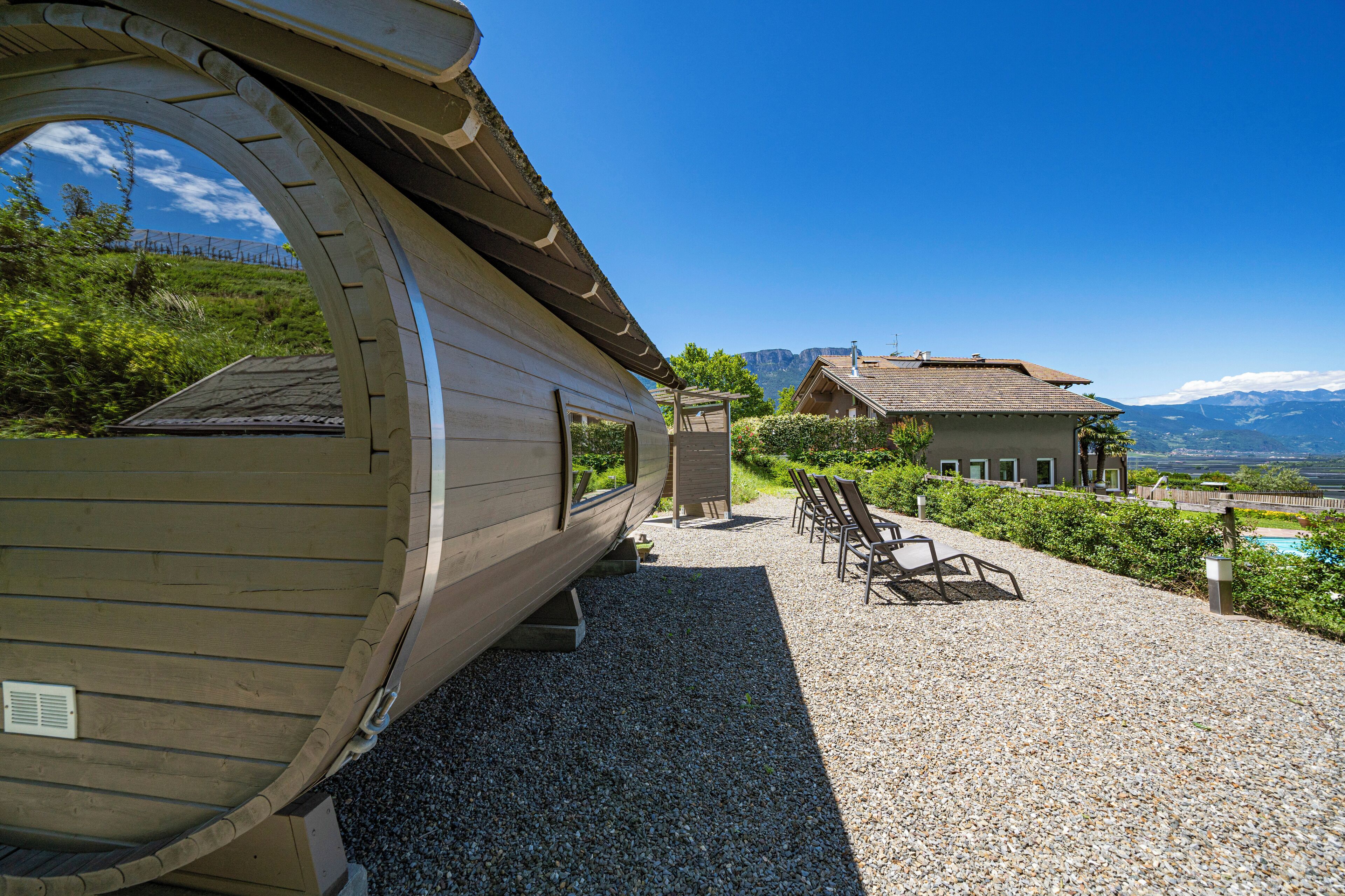 A wooden cabin with a curved roof, a gravel patio, outdoor seating, and a mountain view.