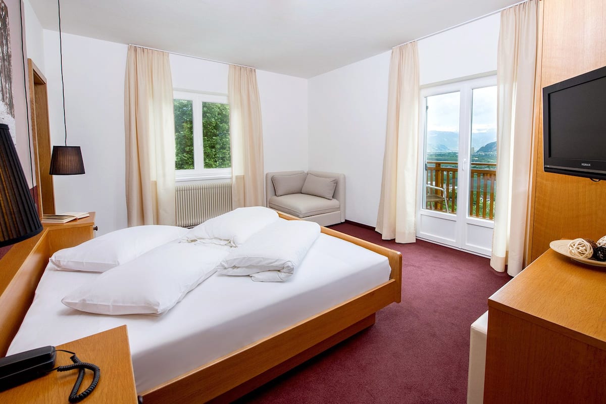 A hotel room with a bed, a chair, a television, and a view of the outdoors.