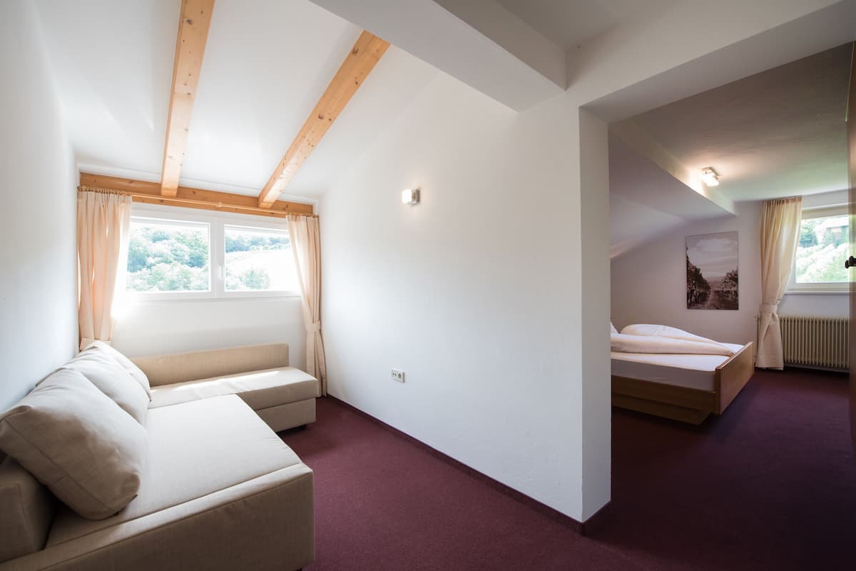 A bedroom with a bed, a sofa, and a window with curtains.