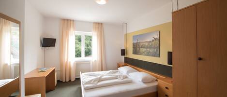 A hotel room with a bed, a desk, a TV, a wardrobe, and a window with curtains.