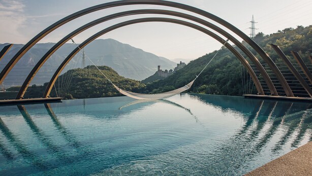 A hammock over a clear pool with a mountainous landscape in the background.