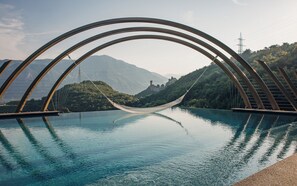 A hammock over a clear pool with a mountainous landscape in the background. - Hotel Sigmundskron (Appiano Sulla Strada del Vino)