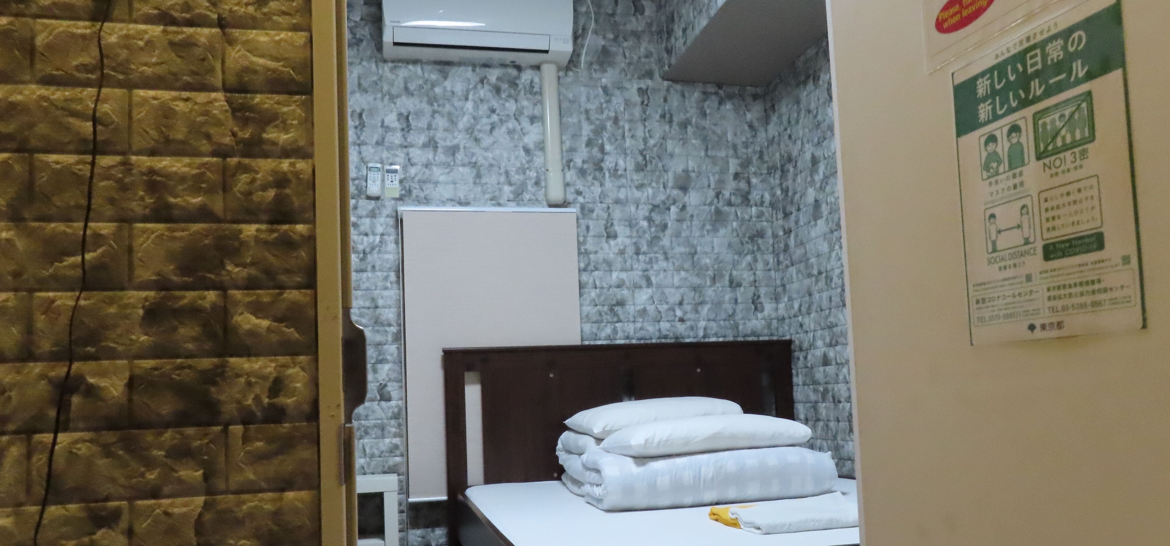 A hotel room with a bed, a white wardrobe, and a wall-mounted air conditioner.
