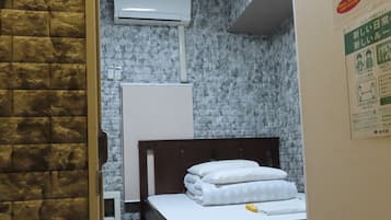 A hotel room with a bed, a white wardrobe, and a wall-mounted air conditioner.
