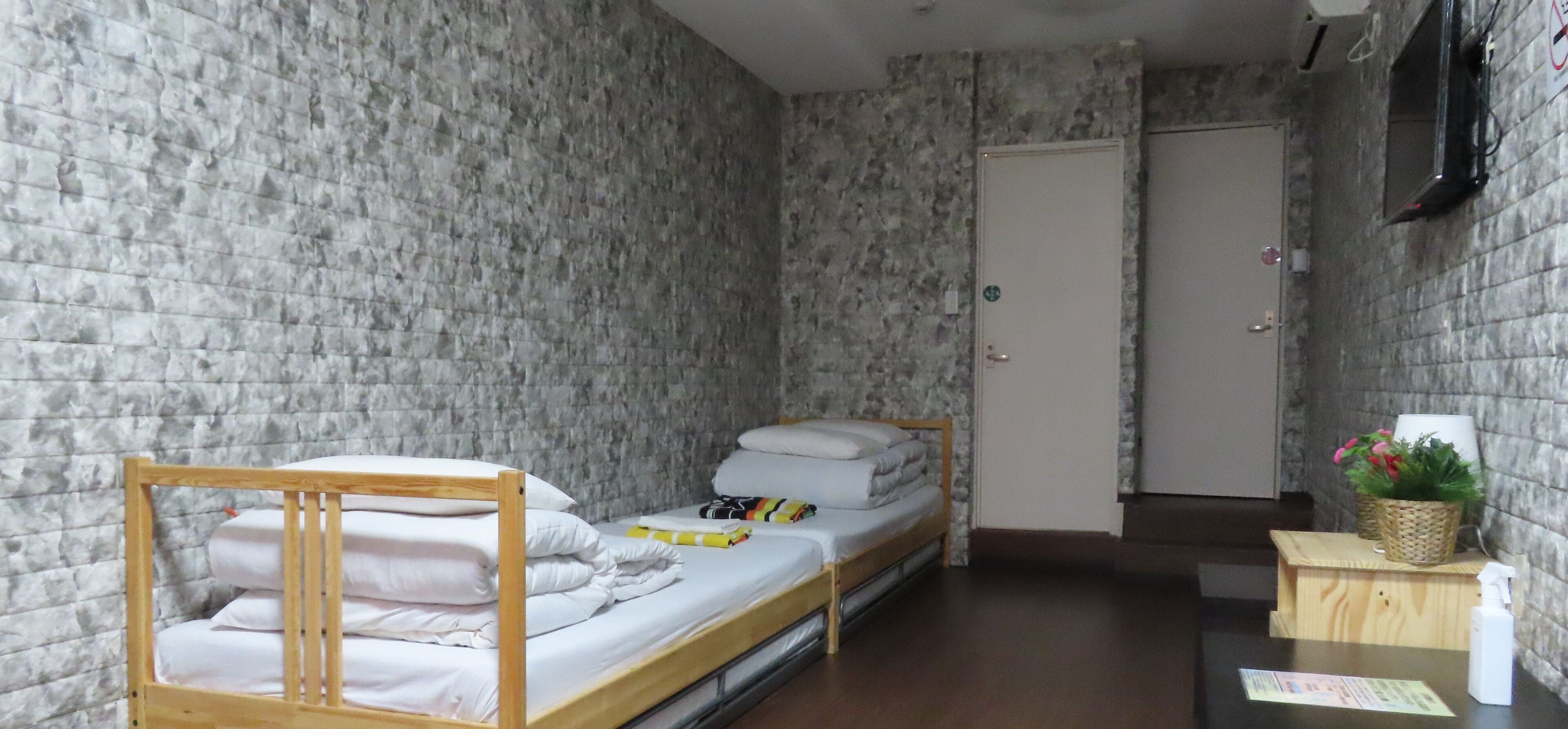 A small, narrow room with a bunk bed, a wooden table with a plant and a spray bottle, and a door with a sign.