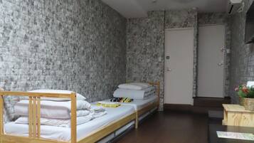A small, narrow room with a bunk bed, a wooden table with a plant and a spray bottle, and a door with a sign.