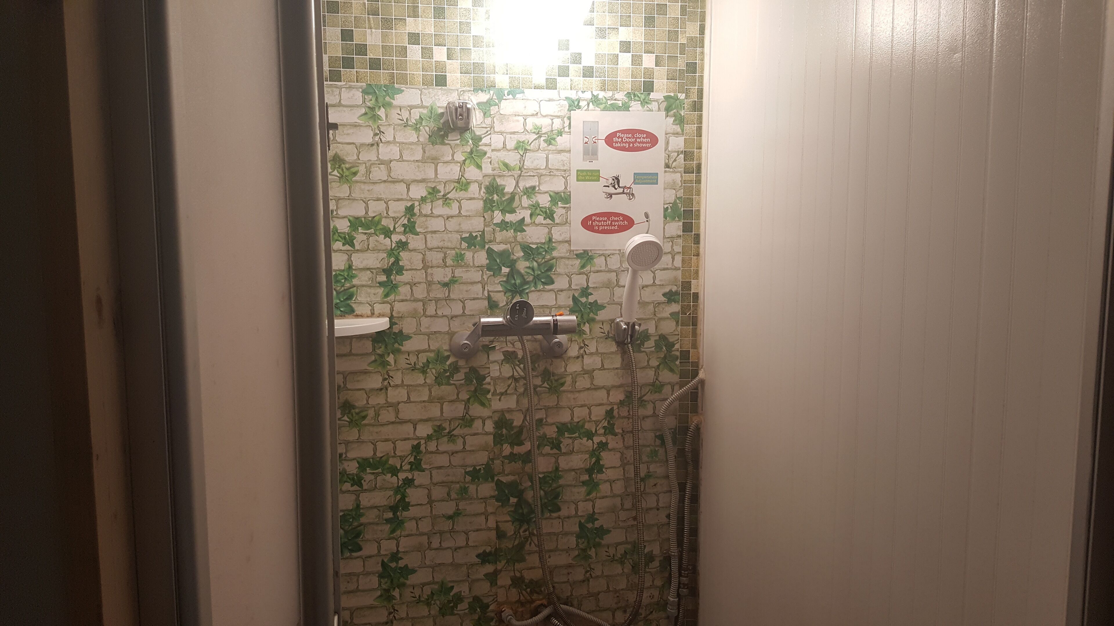 Zona de ducha con pared de azulejos, ducha de mano y grifo empotrado.