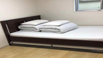 A single bed with a dark headboard and white bedding in a room with light-colored walls and a window.