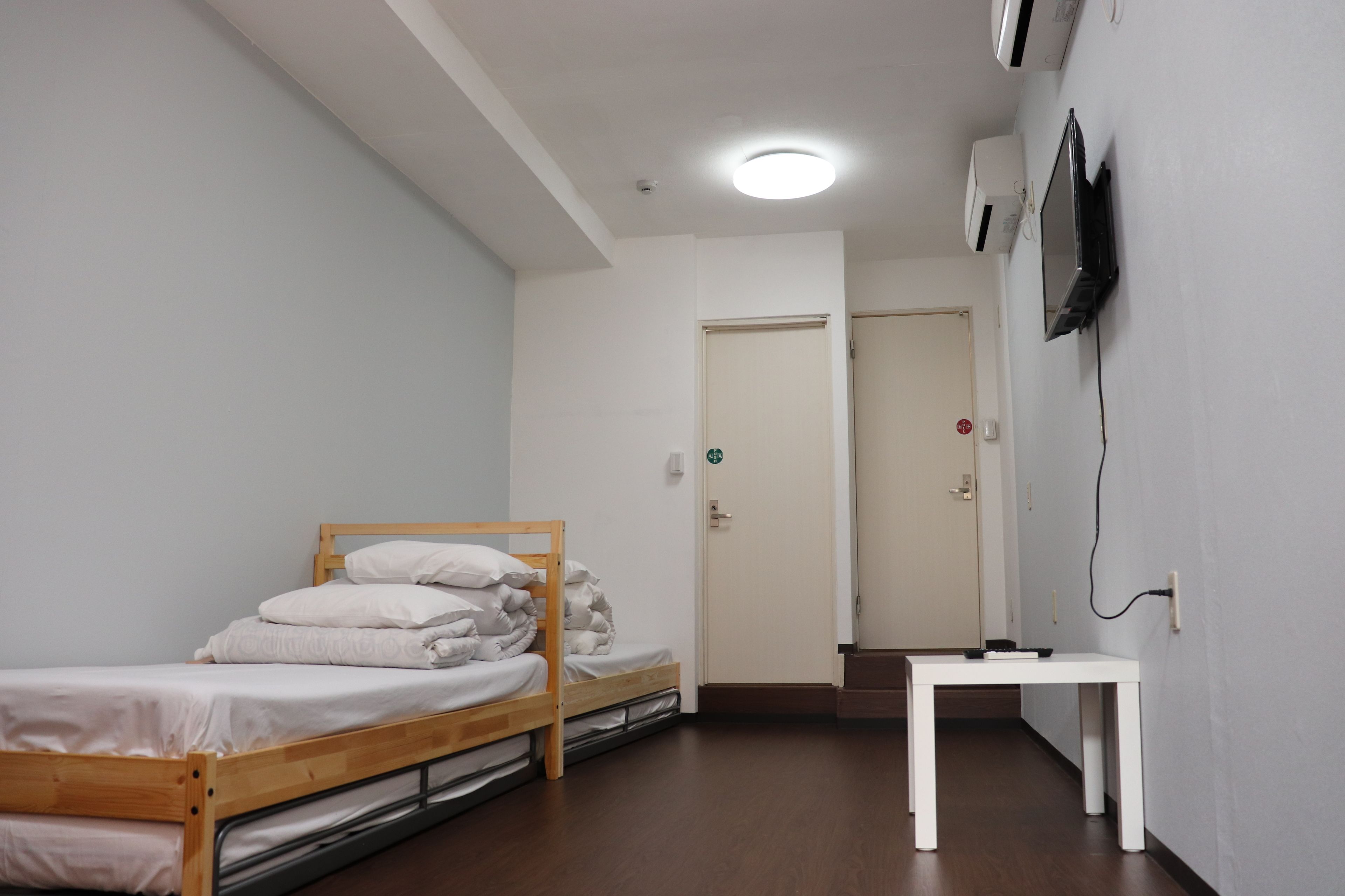Una habitación pequeña y limpia con una cama individual, una mesa blanca y un televisor montado en la pared.