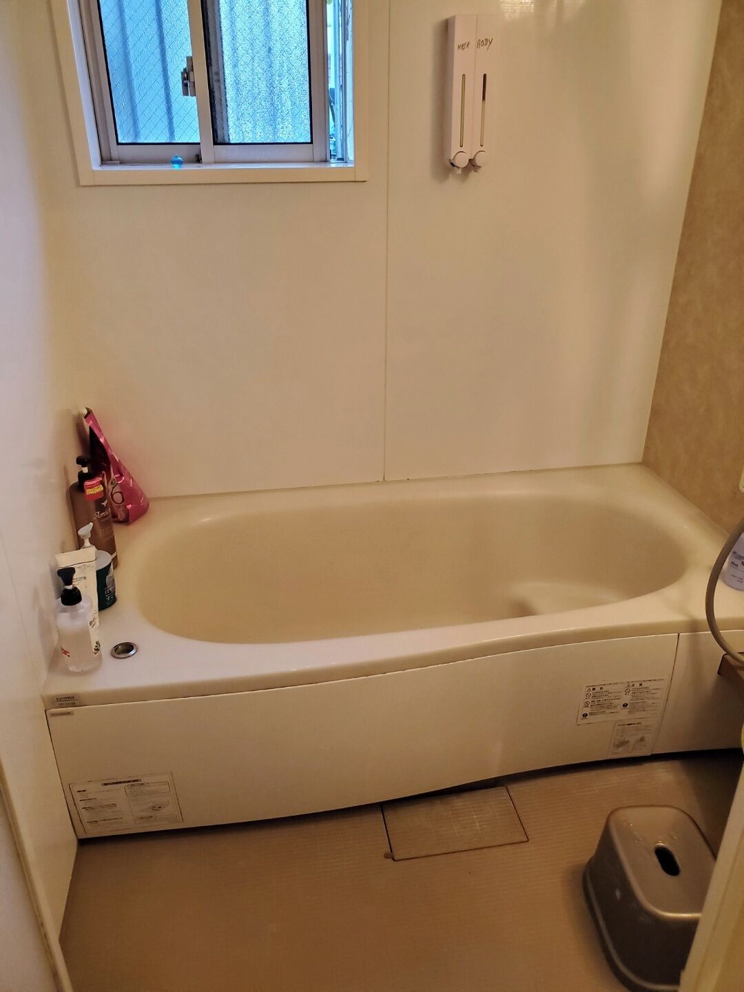 A bathroom with a bathtub, a window, a hand dryer, and a toilet.