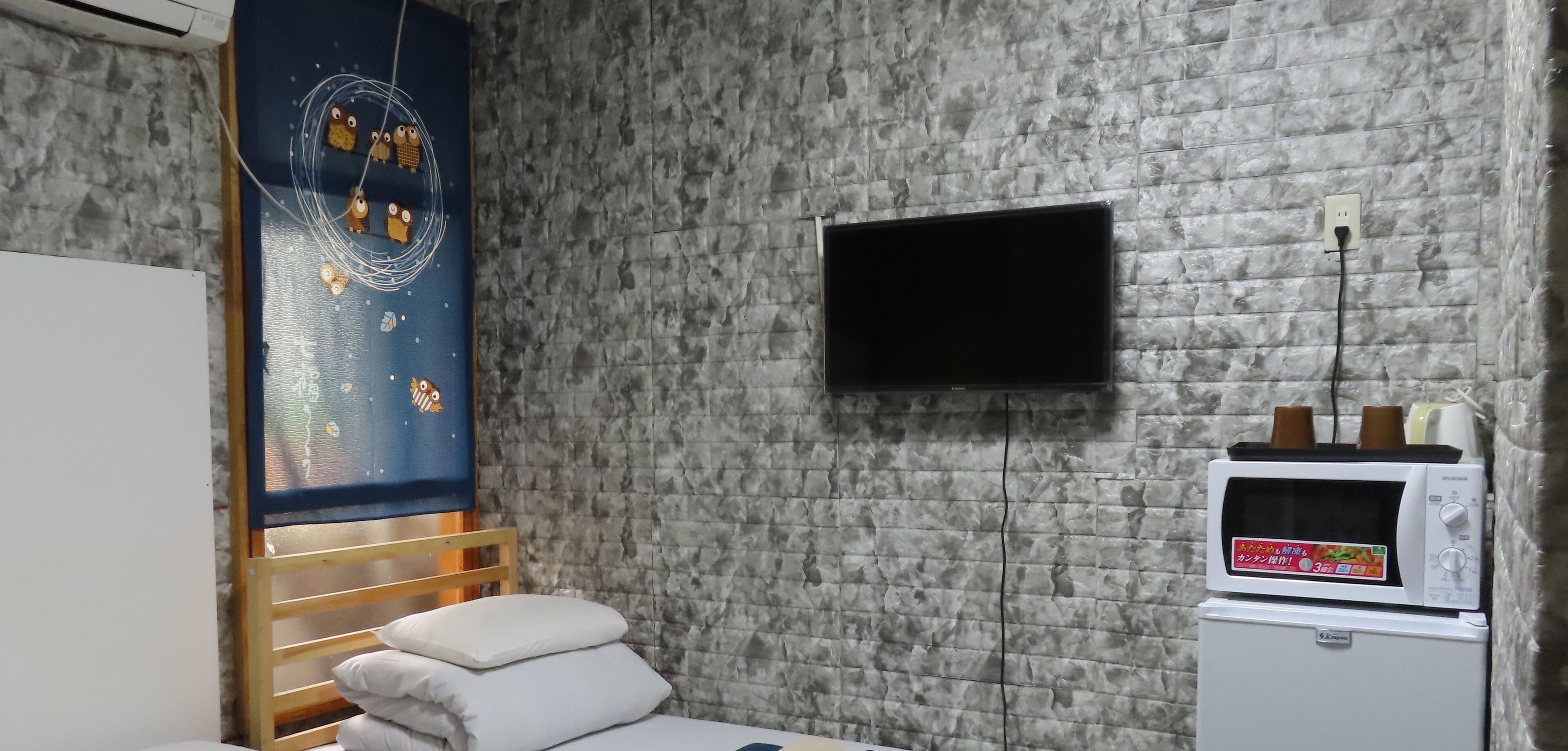 A room with a bed, a wall-mounted TV, a microwave, and a decorative wall panel.