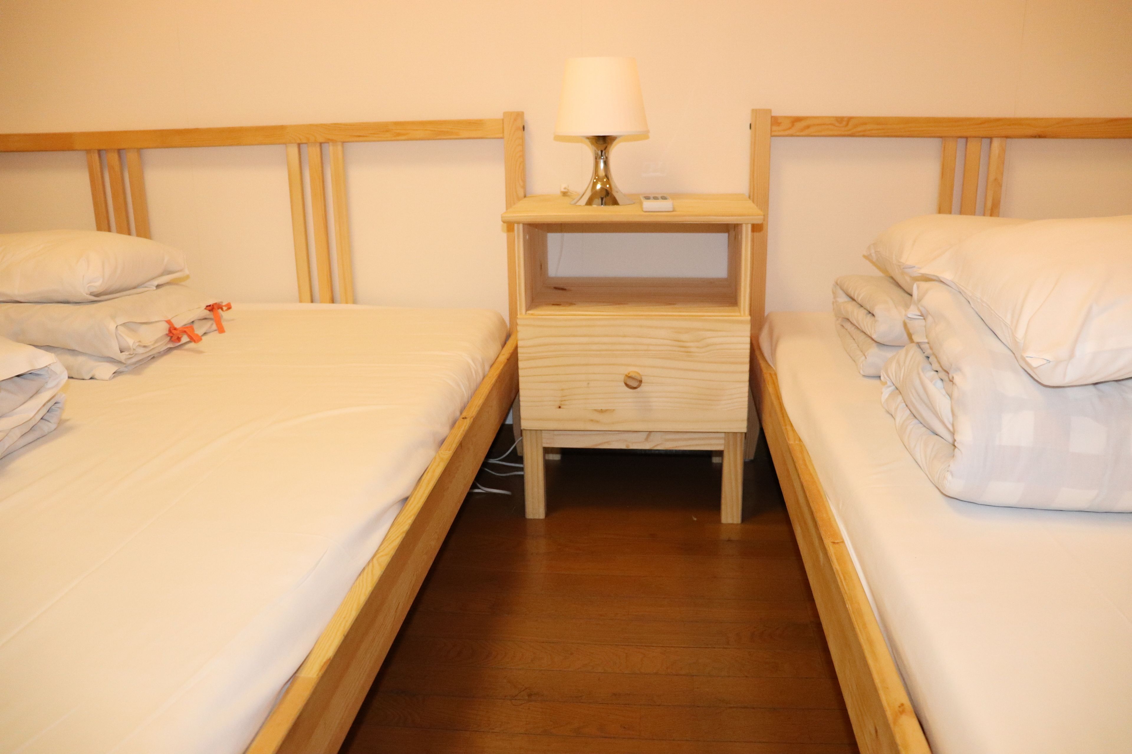 A double room with two beds, each with white bedding and pillows, a wooden headboard, and a bedside table with a lamp.