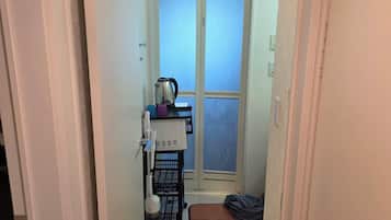 A narrow hallway leading to a room with a window, a kettle, a coffee machine, and a small rug.