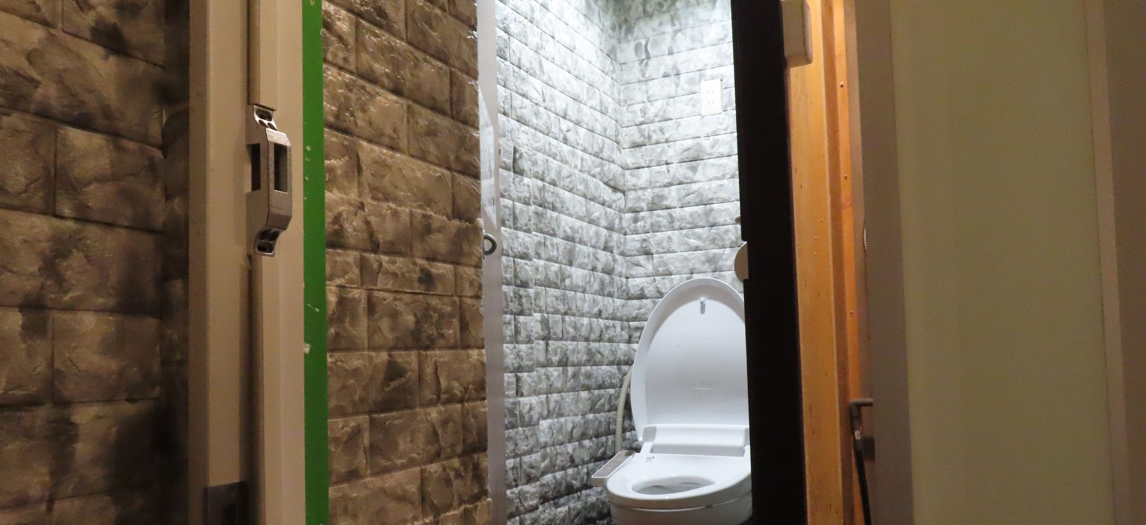 Un baño con inodoro blanco, una línea de seguridad verde y una pared con textura.