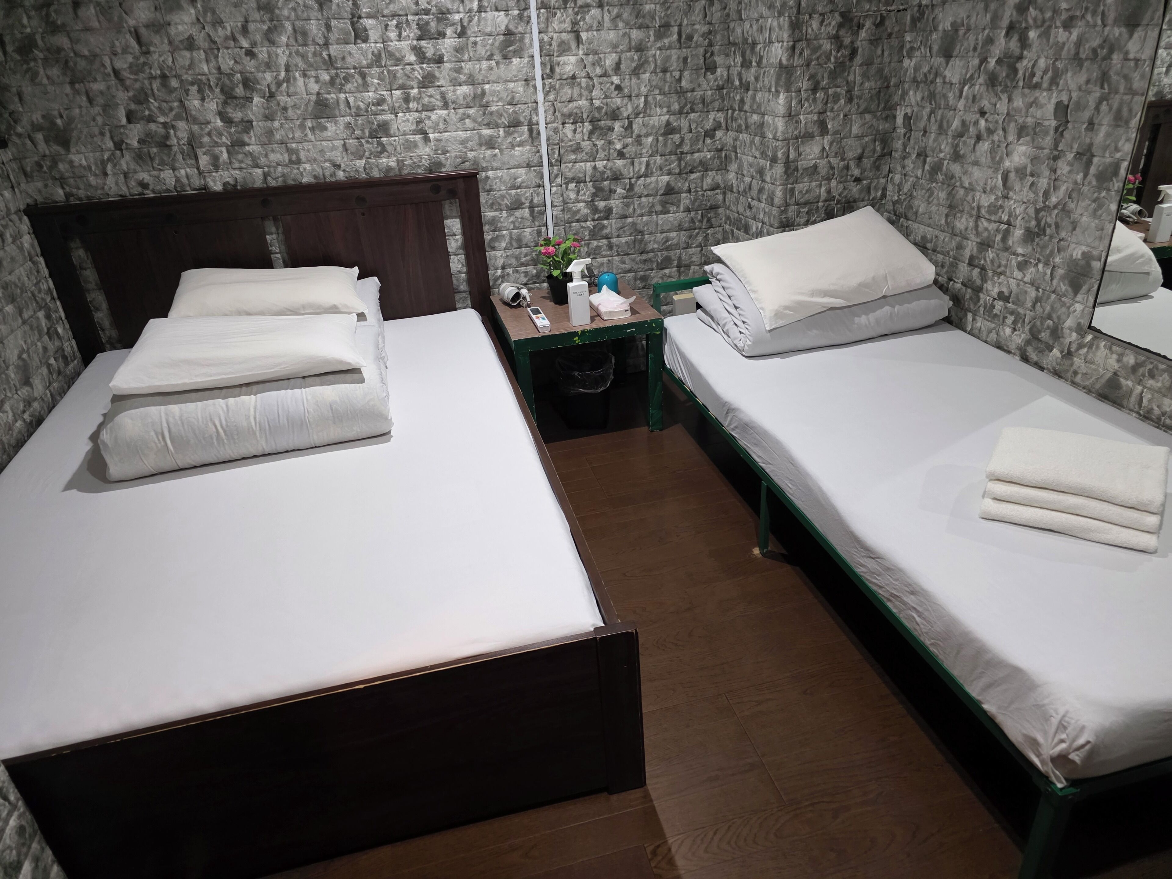 Ein Hotelzimmer mit zwei Betten, einem Holzkopfteil, einem kleinen Nachttisch, einem Spiegel und einer Wand mit Steinoptik.