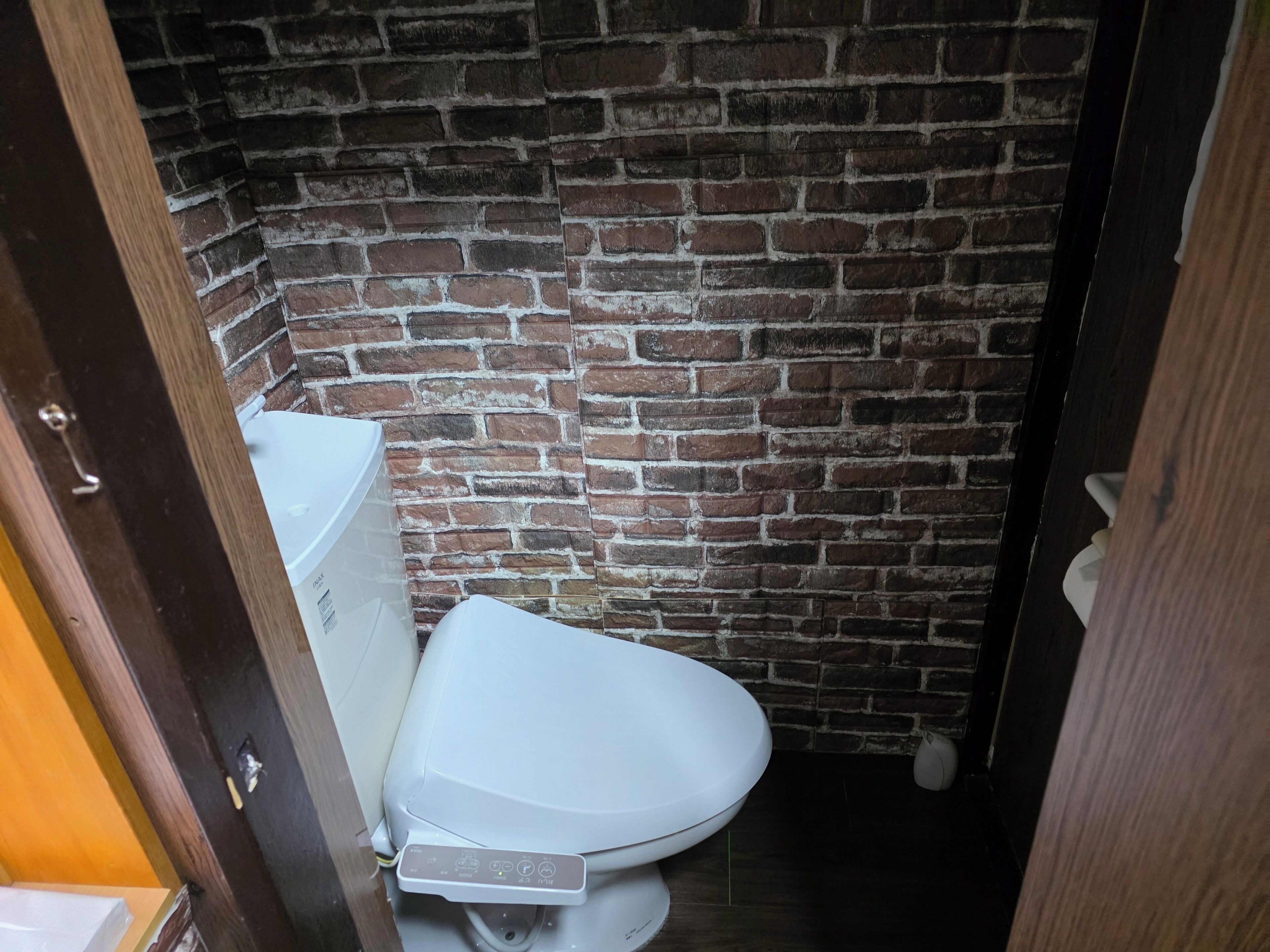 Un baño pequeño y estrecho con inodoro y lavamanos blancos, y pared de ladrillo.