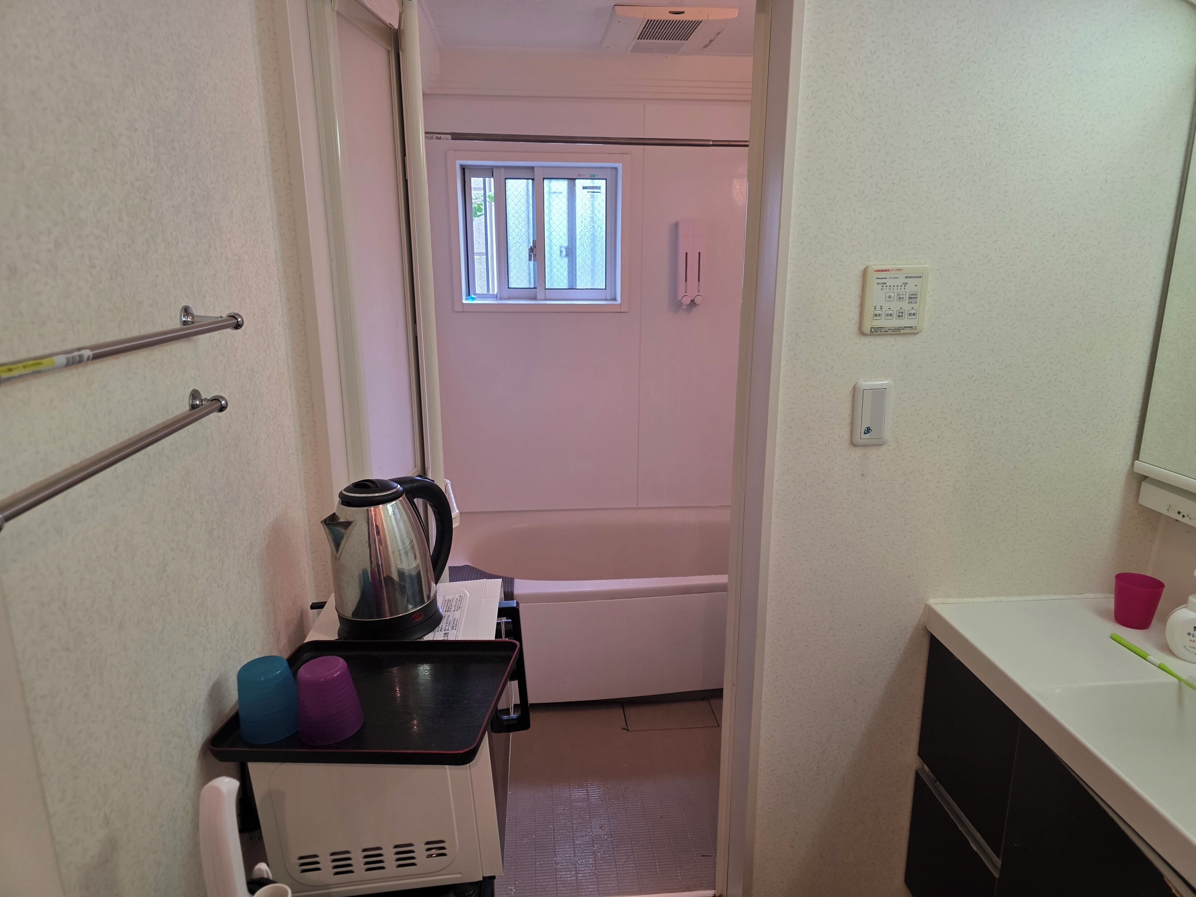 Un baño pequeño con ducha, un perchero, una tetera y una bandeja con tazas.