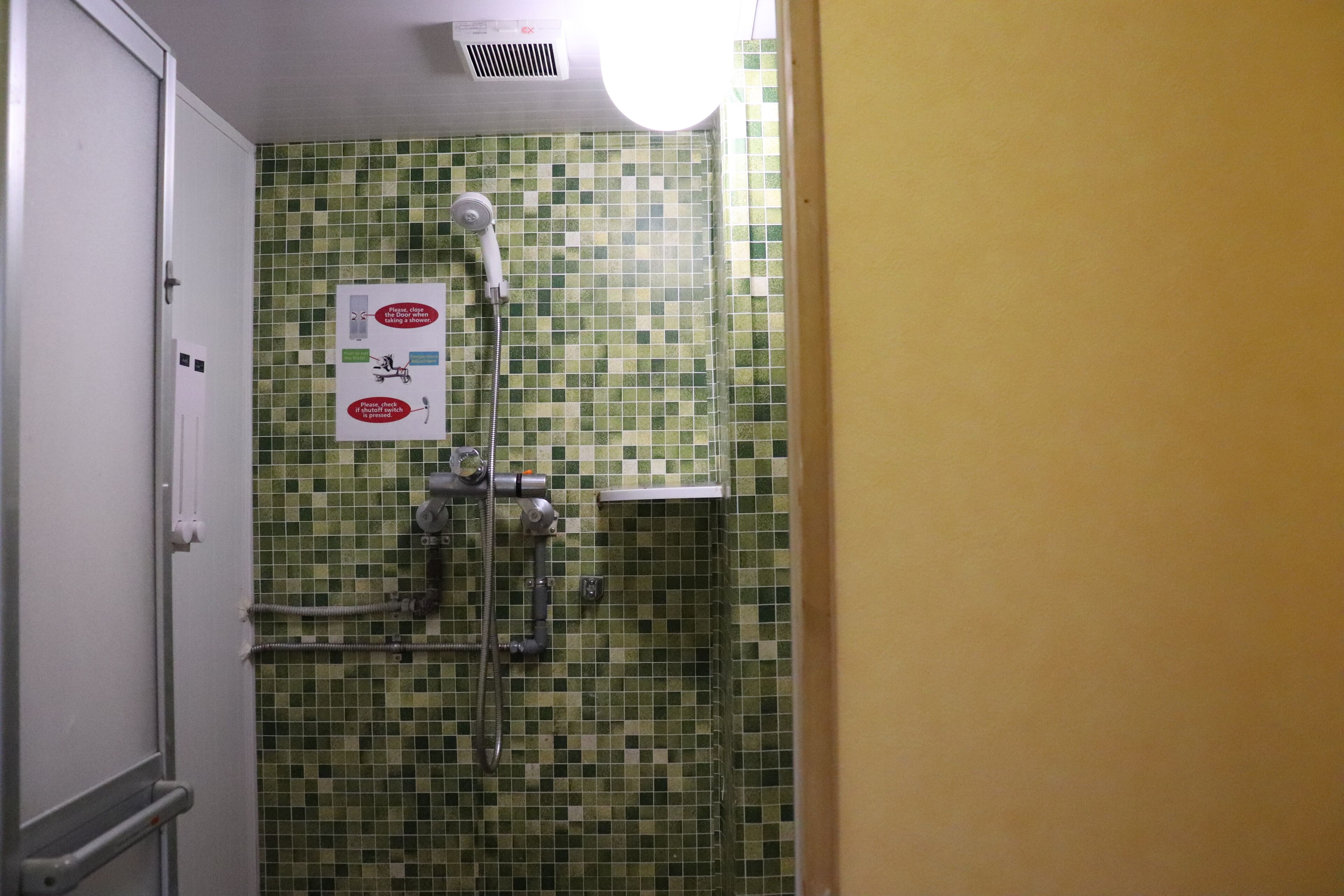 Una ducha con azulejos decorativos, un secador de manos y un cartel con instrucciones de seguridad.