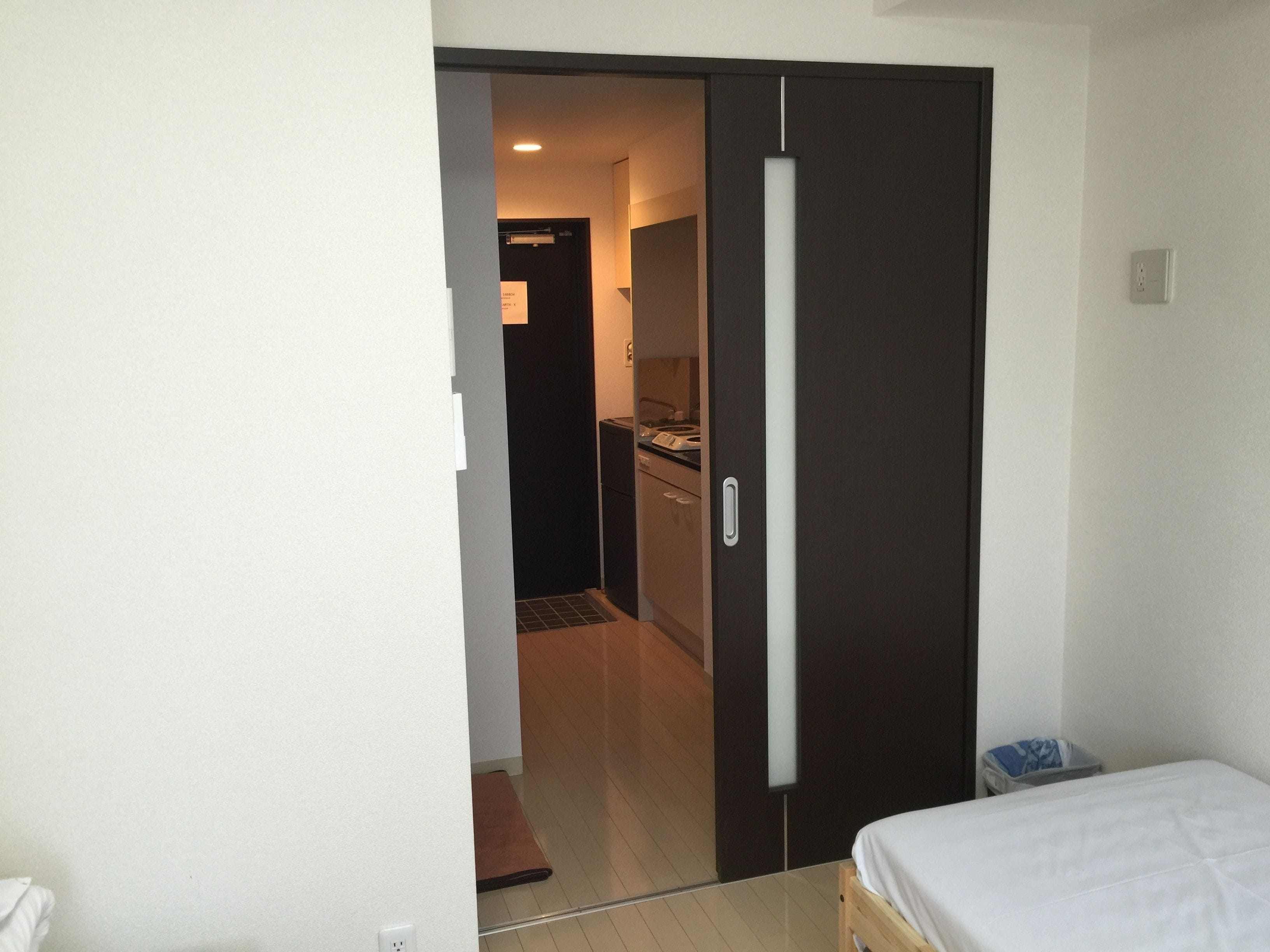 A bedroom with a bed, a wardrobe, and a view into a kitchen area.