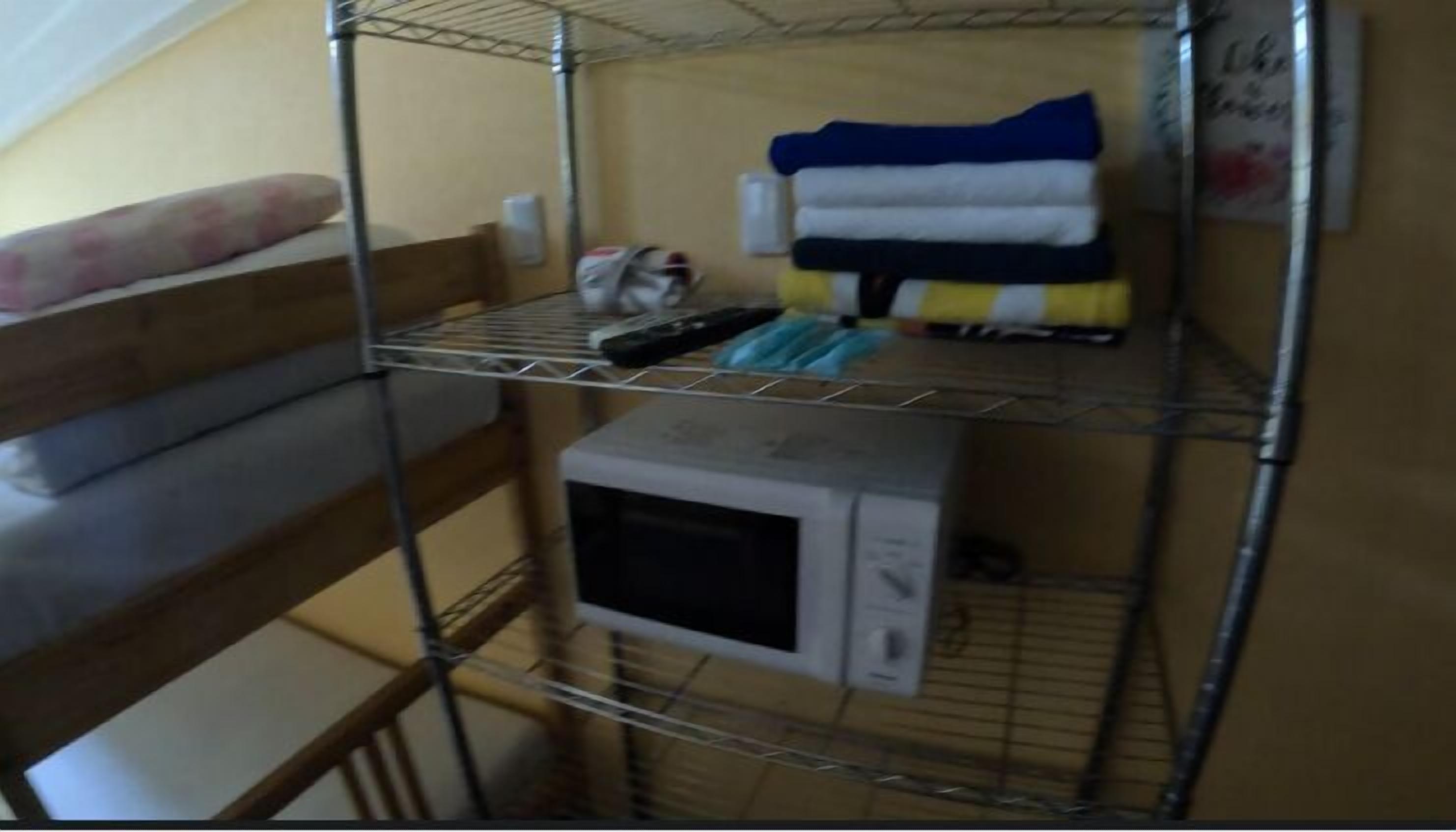 Un lit superposé avec une étagère en métal au-dessus, sur laquelle sont posés un four à micro-ondes et quelques serviettes pliées.
