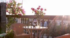 A wicker chair and table with a vase of pink flowers, a bottle of wine, and a glass of red wine on a balcony with a view. - Green Grass Homestay (Hoi An)