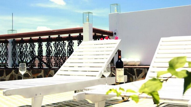 A rooftop terrace with white lounge chairs, a bottle of wine, and a glass of wine on a table. - Green Grass Homestay (Hoi An)