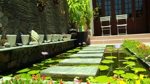 A stone pathway leading to a seating area with chairs, a stone wall with planters, and a water feature with lotus flowers. - Green Grass Homestay (Hoi An)