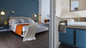 Une chambre à coucher moderne, avec un lit, des lampes de chevet, une table de nuit et une salle de bain équipée d’un lavabo et d’un miroir.