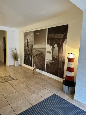 A hotel lobby with a tiled floor, a large wall mural, a potted plant, and a distinctive red and white striped lamp. - Aparthotel kleine Perle (Cuxhaven)
