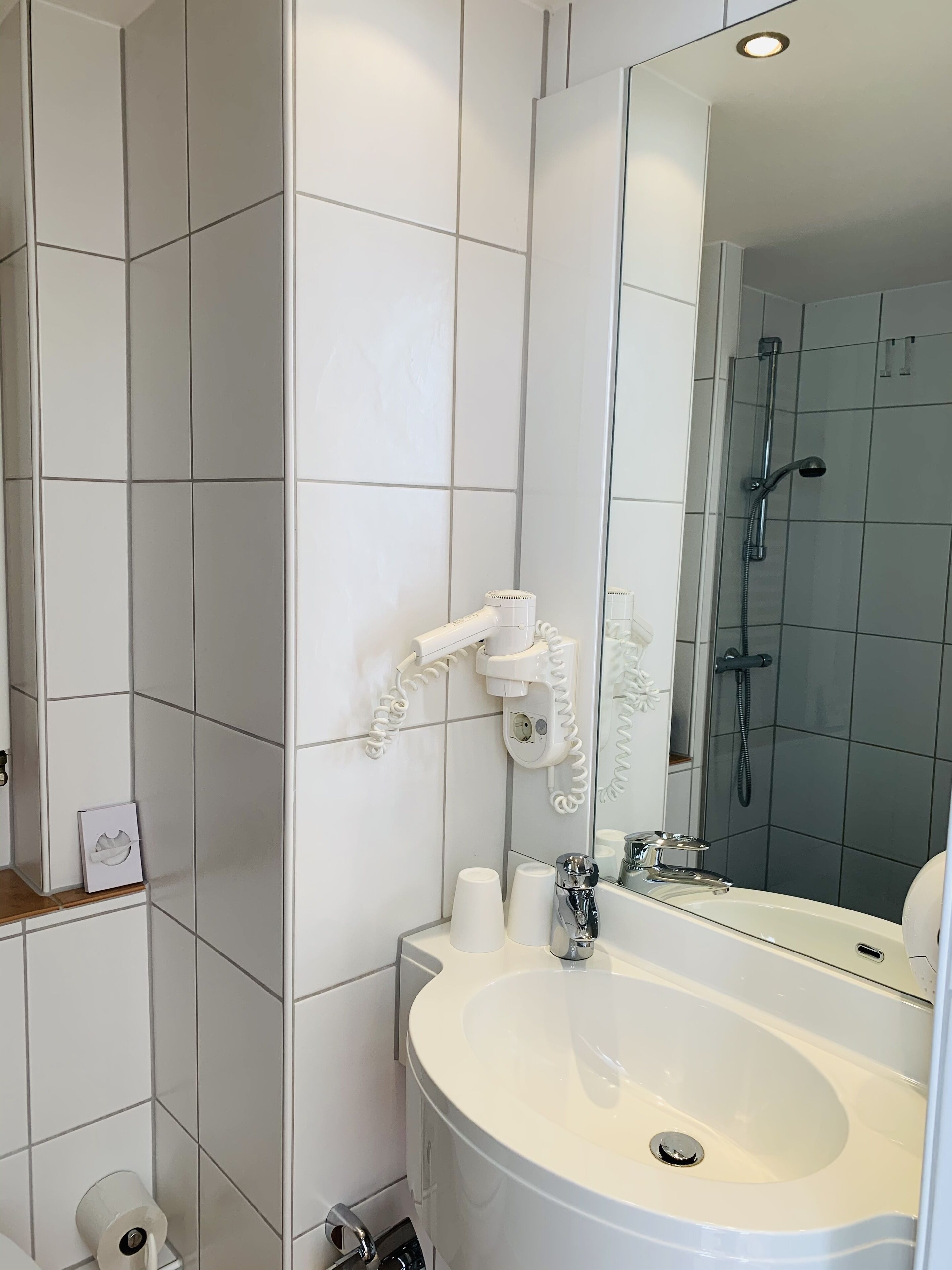 Ein Badezimmer mit weißen Fliesen, einem großen Spiegel, einem Waschbecken und einer Duschkabine.
