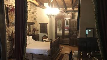 A traditional bedroom with a stone wall, a wooden bed, a chandelier, and a mirror.