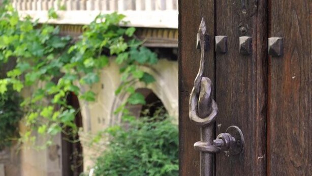 A wooden door with a metal handle and lock, leading to a stone building with a balcony and greenery. - Hotel Palacio de Trasvilla (Villafufre)
