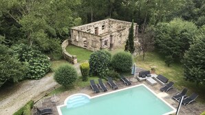 An outdoor swimming pool with lounge chairs and a stone building in the background. - Hotel Palacio de Trasvilla (Villafufre)