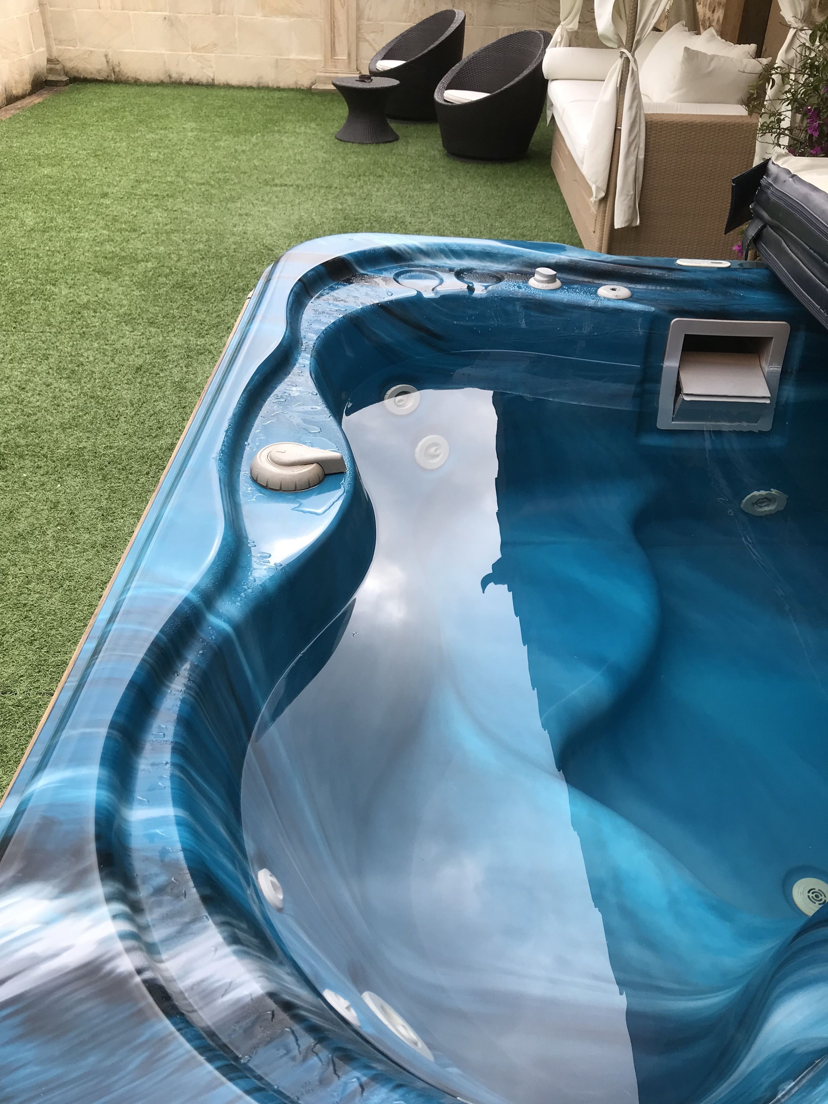 A hot tub with a clear water surface, a small control panel, and a drain plug.