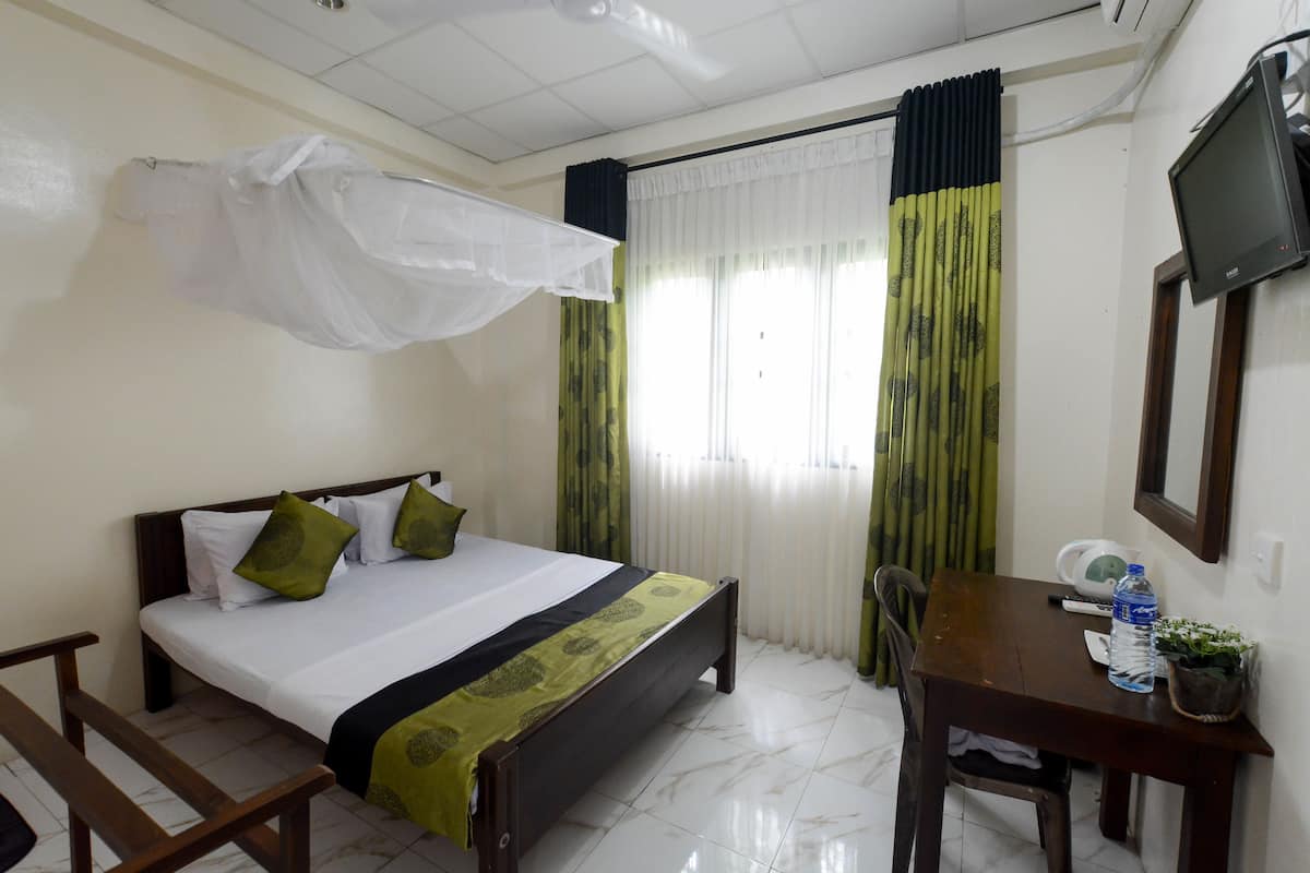 A hotel room with a bed, a desk, a chair, a television, and a window with curtains.