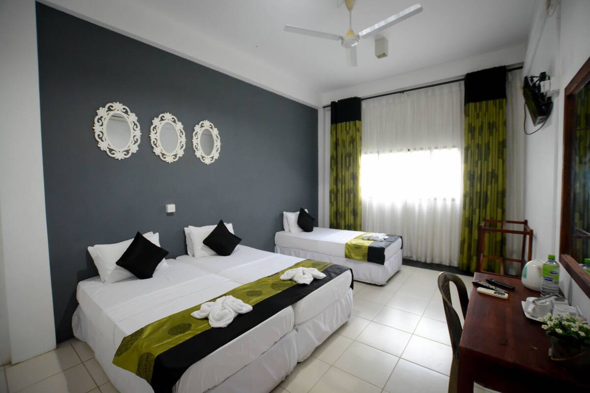 A hotel room with two beds, a dining table, and a ceiling fan.