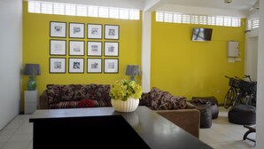 Un salon avec un mur jaune, un canapé, une table basse ornée d’un vase de fleurs et un téléviseur fixé au mur.