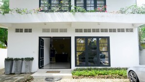 Un bâtiment moderne à deux étages, doté d’une façade blanche, de grandes fenêtres et d’un espace d’entrée pavé.