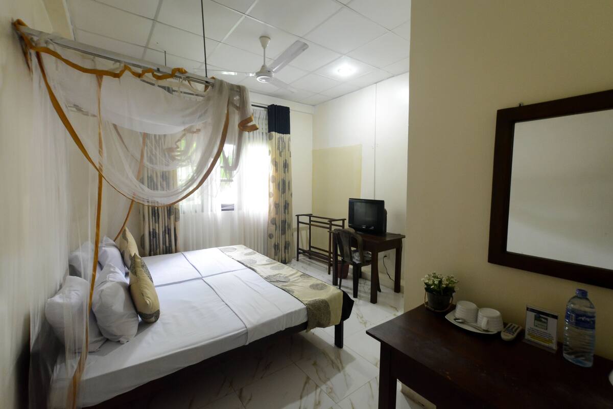 A bedroom with a bed, a desk, a television, and a water bottle.