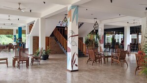 Un espacio interior amplio con una escalera, sillas de madera y plantas en macetas.